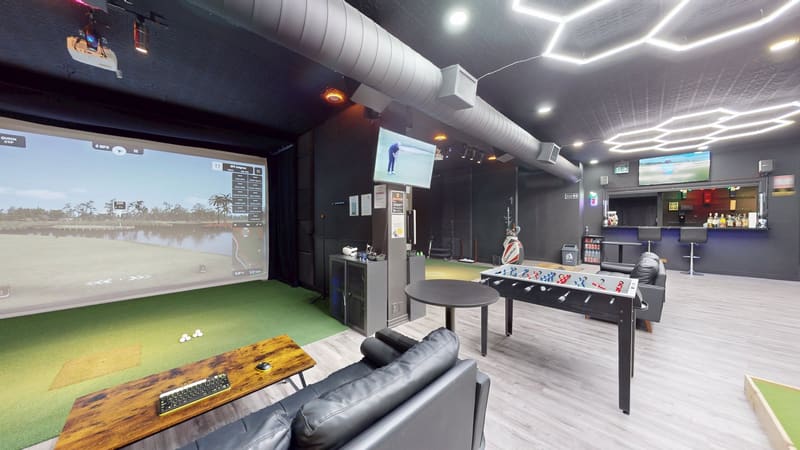 Bay 1 at Club X Indoor Golf, Aurora — TrackMan in play with lounge seating and foosball, hex-lit ceiling
