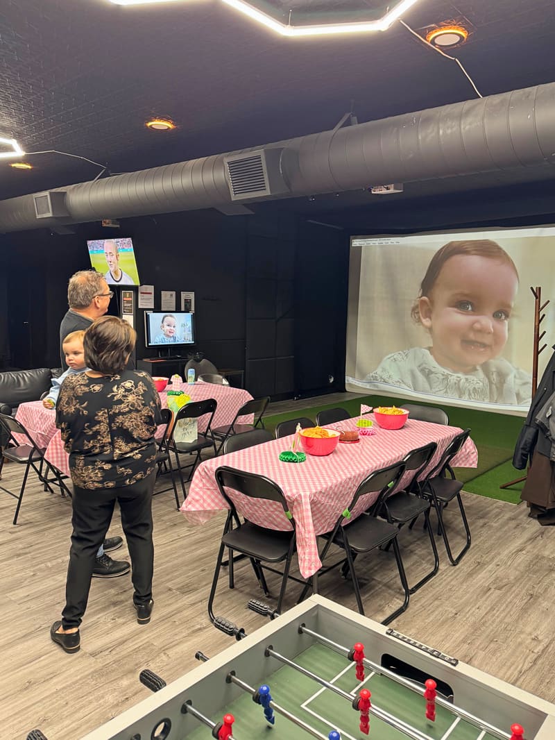 Kids' birthday setup at Club X Indoor Golf — HOLE IN ONE banner backdrop, pink balloons, gift table