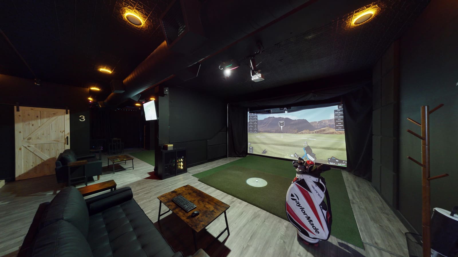 Lounge view at Club X Indoor Golf — sofa, simulator, and TaylorMade golf bag