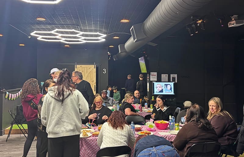 Real private event at Club X Indoor Golf, Aurora — adults seated at tables under the hex-lit ceiling